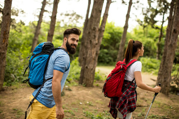 Couple of young happy travelers hiking with backpacks on the beautiful forest trail