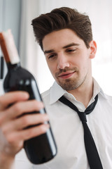 Photo of unshaved brunette businessman holding bottle of wine in hotel apartment