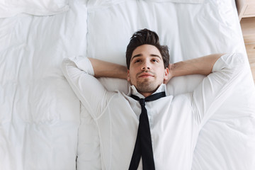 Photo from top of european calming businessman lying on bed in hotel apartment