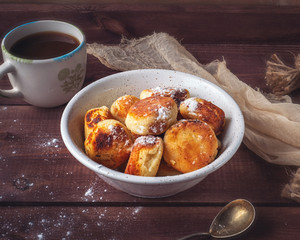 Breakfast with homemade cheesecakes with powdered sugar and tea on a wooden tray. Beige napkin and tea complement the composition.