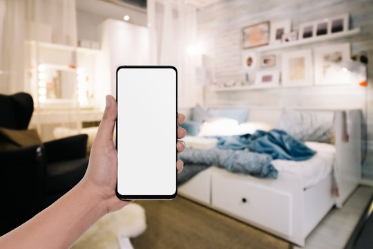 Mockup image of  hand holding modern mobile phone with blank copy space desktop screen for your advertisement in bedroom