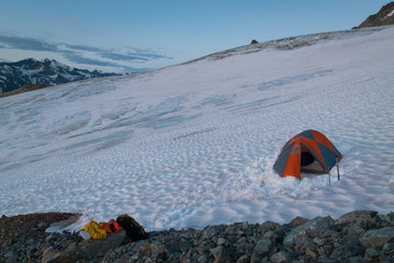 Orange mountaineering tent on snow in mountains with mountain in the background