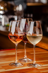 Glasses of white, rose and red wine are on the table, a bottle and corks are nearby. Glasses are on the table in the bar in the restaurant. Background image. copy space