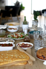 Lavish homemade lunch served on table: focaccia bread, prosciutto, porchetta, mozzarella cheese, pesto, caponata, caramelized onion, with arugula and cherry tomato salad. Selective focus.