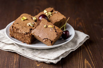 Three Pieces of Tasty Homemade Chocolate Brownies on White Plate Decorated with Cherry and Pistachios Wooden Background Homemade Bakery and Dessert Copy Space