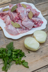 Recipe for a festive meal and a healthy diet. Carcasses of domestic rabbit, cut into pieces, raw meat with spices and vegetables on a plate on a wooden background of boards. magazine cover, flatlay