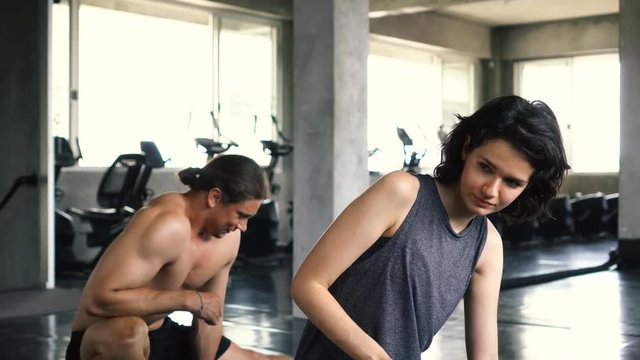 Young woman and man stretching their legs on the gym floor. Two people couple working out indoors