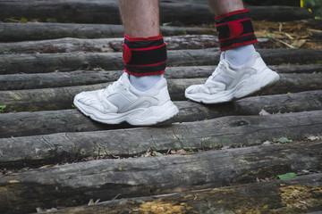 Fototapeta na wymiar human legs standing on a wooden raft in white sneakers with red weighting