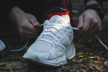 man tying shoelaces in his white sneakers with weights on his feet