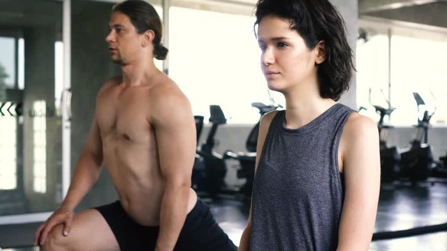 Young woman and man stretching their legs on the gym floor. Two people couple working out indoors