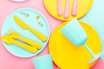 Bright colored plastic picnic utensils. Pink, yellow, blue colors in the bowl. Photo in hard light. Copy space