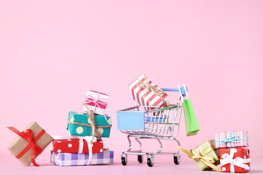 Small Shopping Cart With Gift Boxes On Pink Background