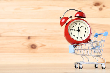 Small shopping cart with alarm clock on brown wooden table