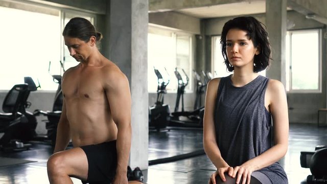 Young woman and man stretching their legs on the gym floor. Two people couple working out indoors