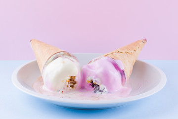 Fototapeta na wymiar Melted ice cream on a pink blue background. Two ice cream cones on a white plate. Summer milk dessert in a waffle cone. Summer concept