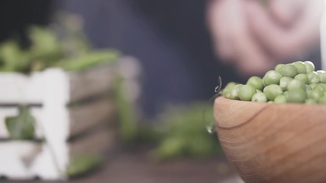 Man's hand breaks a pod of green peas and puts it in a wooden bowl, slow motion. Agricultural concept.