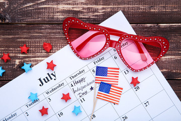Text Happy Independence Day in calendar with american flags and sunglasses on wooden table