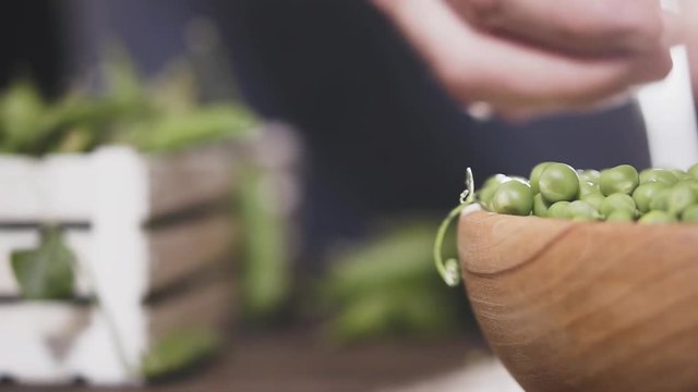 Man's hand breaks a pod of green peas and puts it in a wooden bowl, slow motion. Agricultural concept.