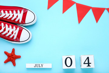 Independence Day on calendar with starfish, sneakers and paper flags on blue background