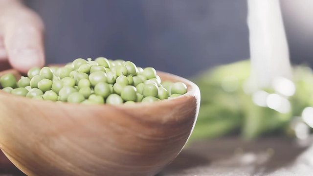 Farmer's hand puts wooden bowl of green peas on table, close-up, slow motion. Agricultural concept. Eco food.