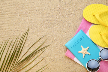 Flip flops with starfish, passport and palm leaf on beach sand