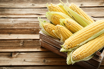 Ripe corn in crate on brown wooden table
