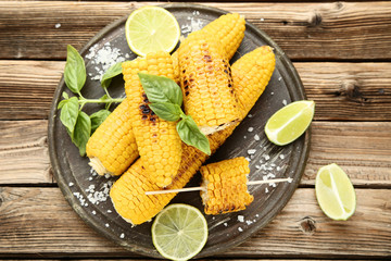 Grilled corn with lime pieces and basil leafs on wooden table