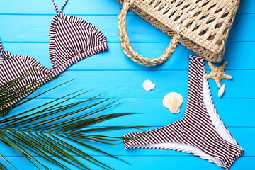 Fashion swimsuit with palm leaf and seashells on blue wooden table