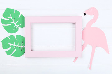 Wooden blank frame with paper green leafs and flamingo on white table