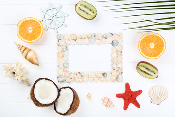 Wooden blank frame with seashells, palm leaf and fruits on white table