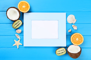 Wooden blank frame with seashells and fruits on blue table