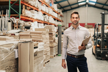 Smiling manager standing in his warehouse with a clipboard