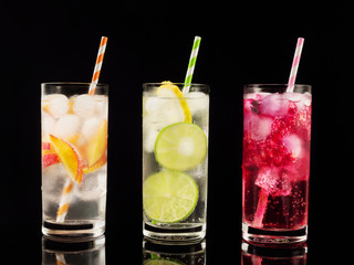 Delicious summer  lemonades with ice,berry, peach and lime on black background. Three glass with cold, fresh drink or coctail on black table