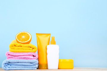 Folded towels with orange fruit and sunscreen bottles on blue background