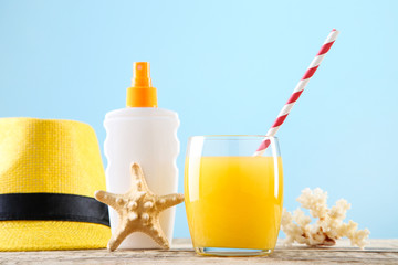 Orange juice with sunscreen, hat and seashells on blue background