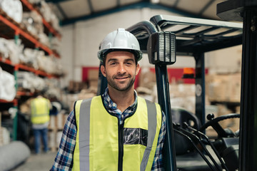Smiling worker standing by his forklift in a warehouse