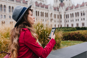 Worried dark-haired girl in gray hat using gps while enjoying attractions. Outdoor photo of stylish...