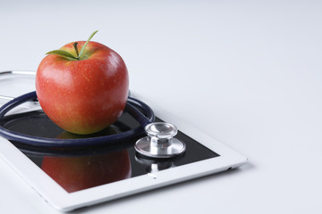 Medical stethoscope and red apple lying on a tablet isolated on white background.