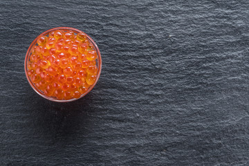 Red caviar in the bowl on gray graphite background. Top view.