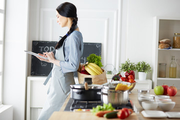 Beautiful young woman using a digital tablet in the kitchen