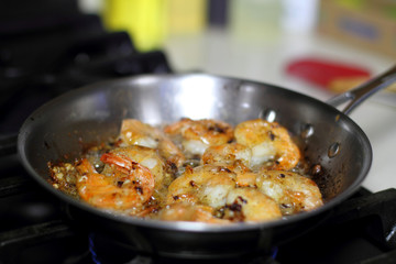 Shrimp scampi cooking in butter and garlic in a stainless steel skillet on the stove.