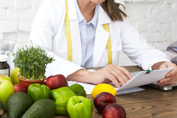 Cropped image of unrecognizable mature female dietician in white medical gown holding pen and...