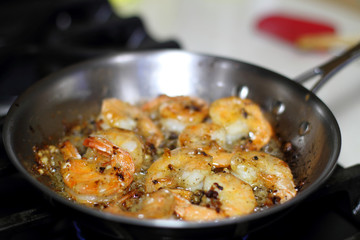 Shrimp scampi cooking in butter and garlic in a stainless steel skillet on the stove.