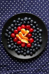 Strawberries, cherries and tangerines on black plate with dotted tablecloth. Top view.