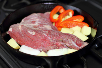 Sirloin tritip steak in a cast iron pan with potatoes and onions on the stove top.