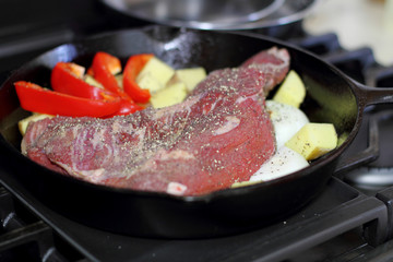 Sirloin tritip steak in a cast iron pan with potatoes and onions on the stove top.