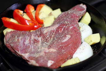 Sirloin tritip steak in a cast iron pan with potatoes and onions on the stove top.