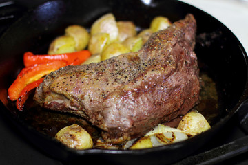 Sirloin tritip steak in a cast iron pan with potatoes and onions on the stove top.