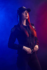 Serious female police officer is posing for the camera against a black background with red and blue backlighting.