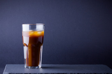 Iced coffee on a dark background. Summer drink with caffeine on the slate board. Iced coffee in a glass. Copy space